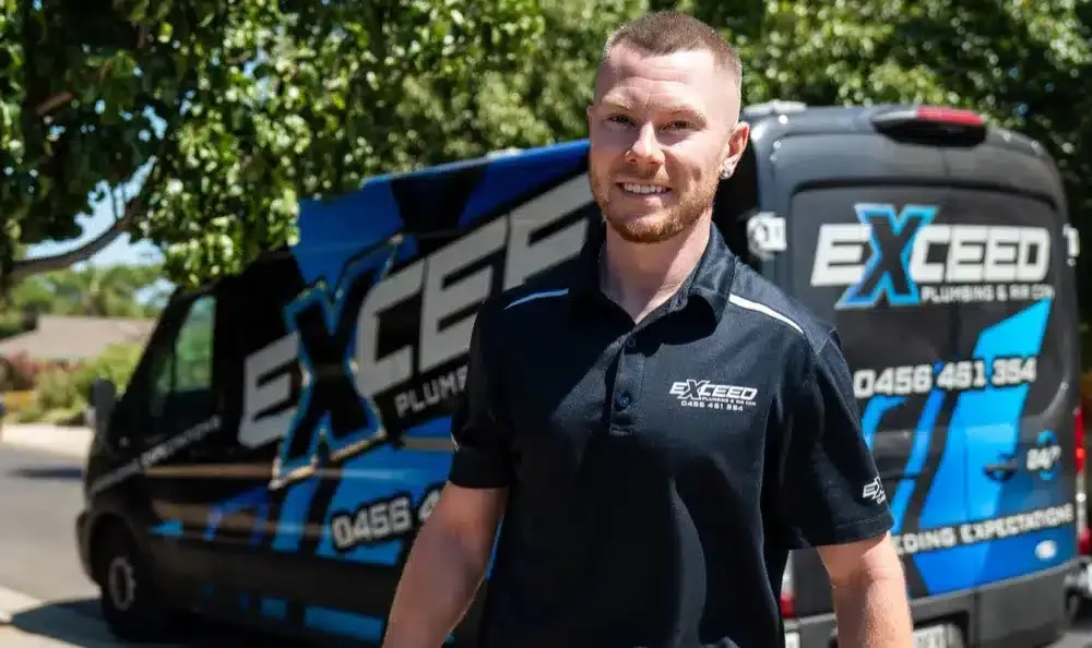Caleb John, owner of Exceed Plumbing, smiling beside the branded service van